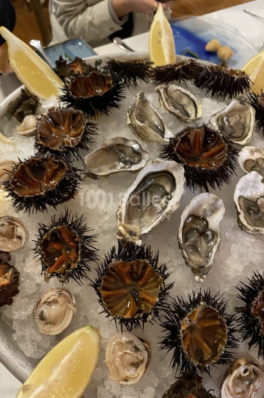 Plateau de fruits de mer avec oursins, huîtres, palourdes et quartiers de citron disposés sur de la glace.