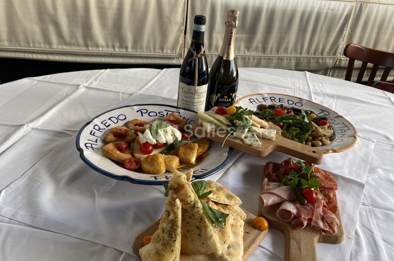 Assortiment de plats italiens avec charcuterie, fromages, légumes, pain et bouteilles de vin sur une table dressée.
