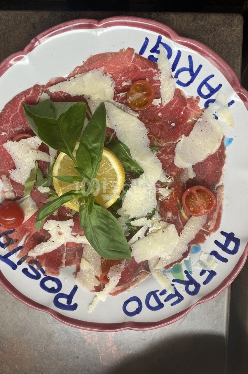 Assiette de carpaccio de bœuf garnie de copeaux de parmesan, tomates cerises, basilic et tranche de citron.
