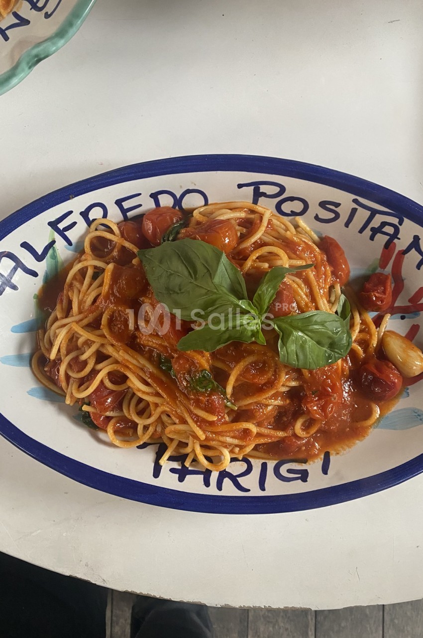 Assiette de spaghetti à la sauce tomate garnie de feuilles de basilic, servie sur une table blanche.