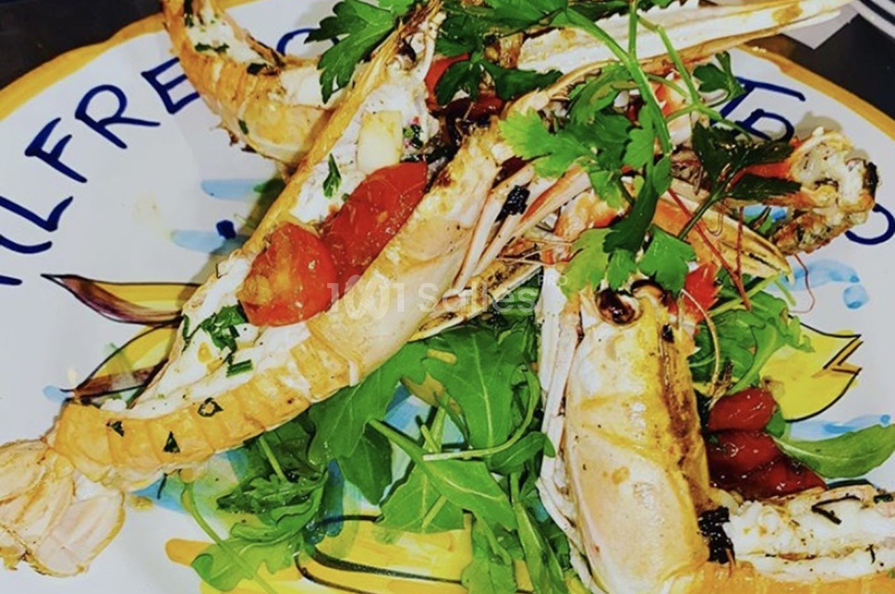 Assiette de langoustines grillées servies sur un lit de roquette avec tomates cerises et herbes fraîches.