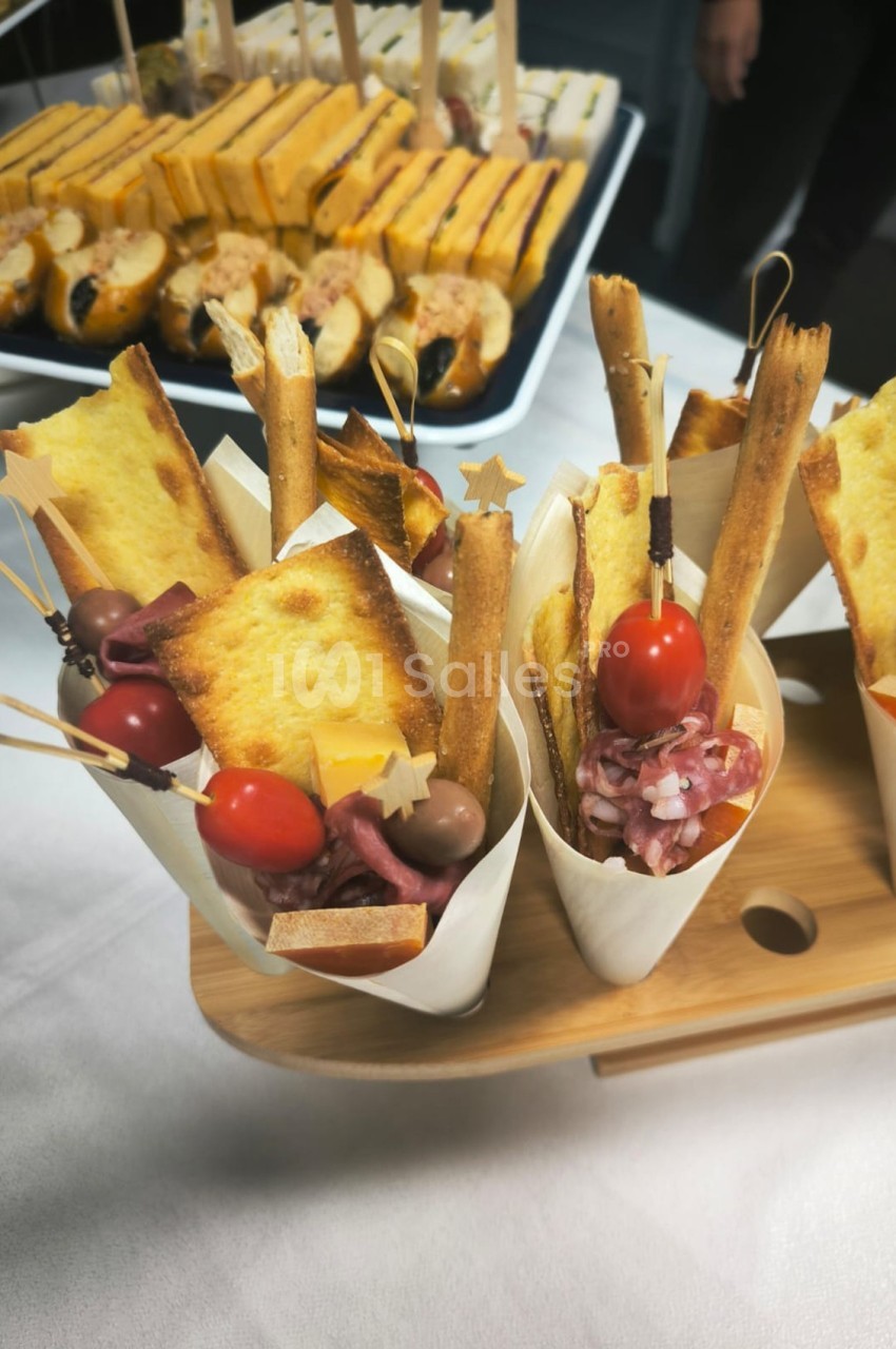 Cornets apéritifs garnis de gressins, tomates cerises, charcuterie et toasts, présentés sur un plateau en bois.