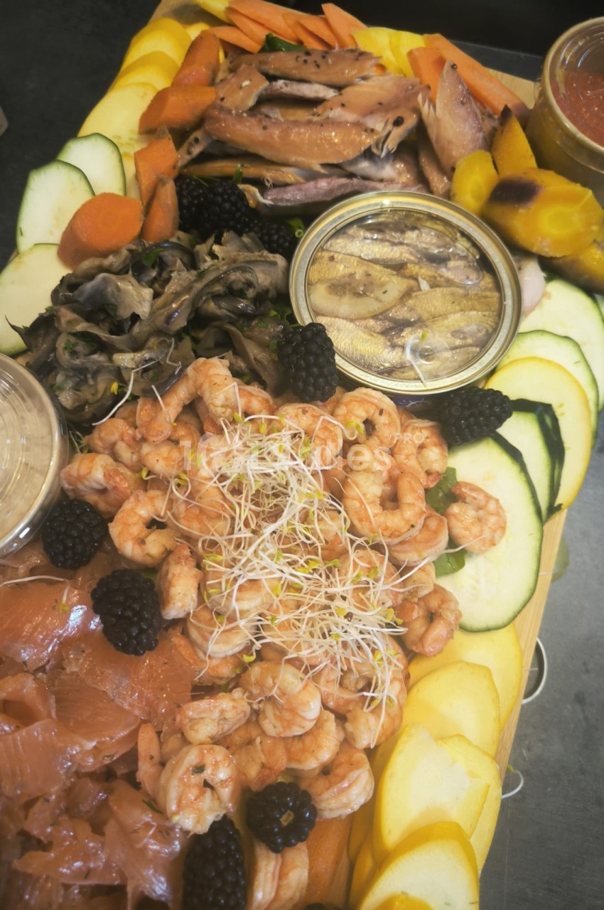 Plateau de fruits de mer avec crevettes, saumon fumé, anchois, légumes frais et condiments variés.