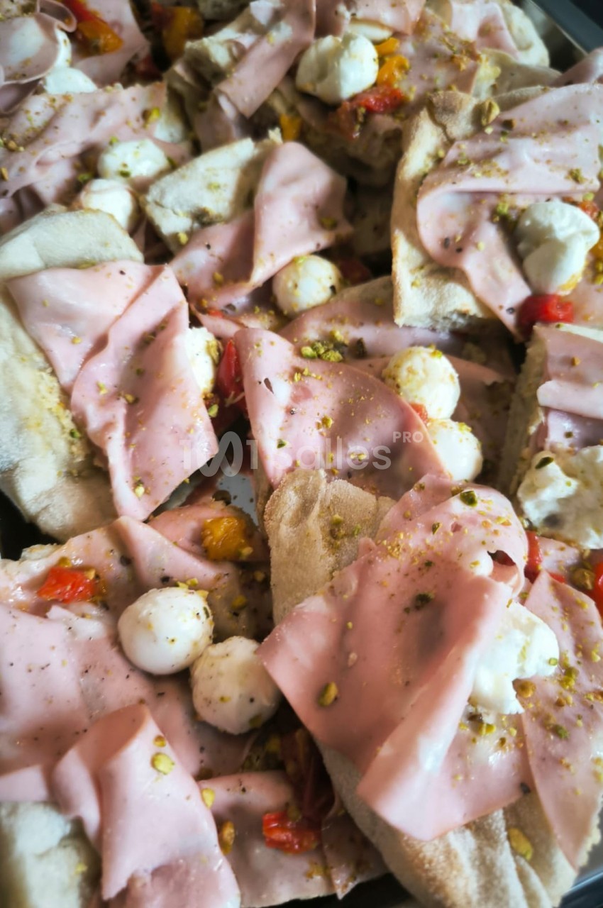 Tranches de focaccia garnies de mortadelle, mozzarella, poivrons grillés et éclats de pistache.