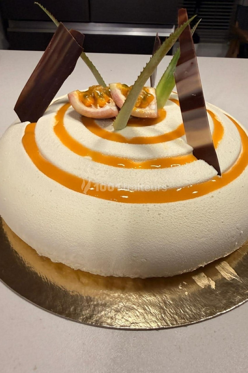 Gâteau rond avec glaçage blanc, décoré de spirales orange, morceaux de fruit de la passion et plaques de chocolat.