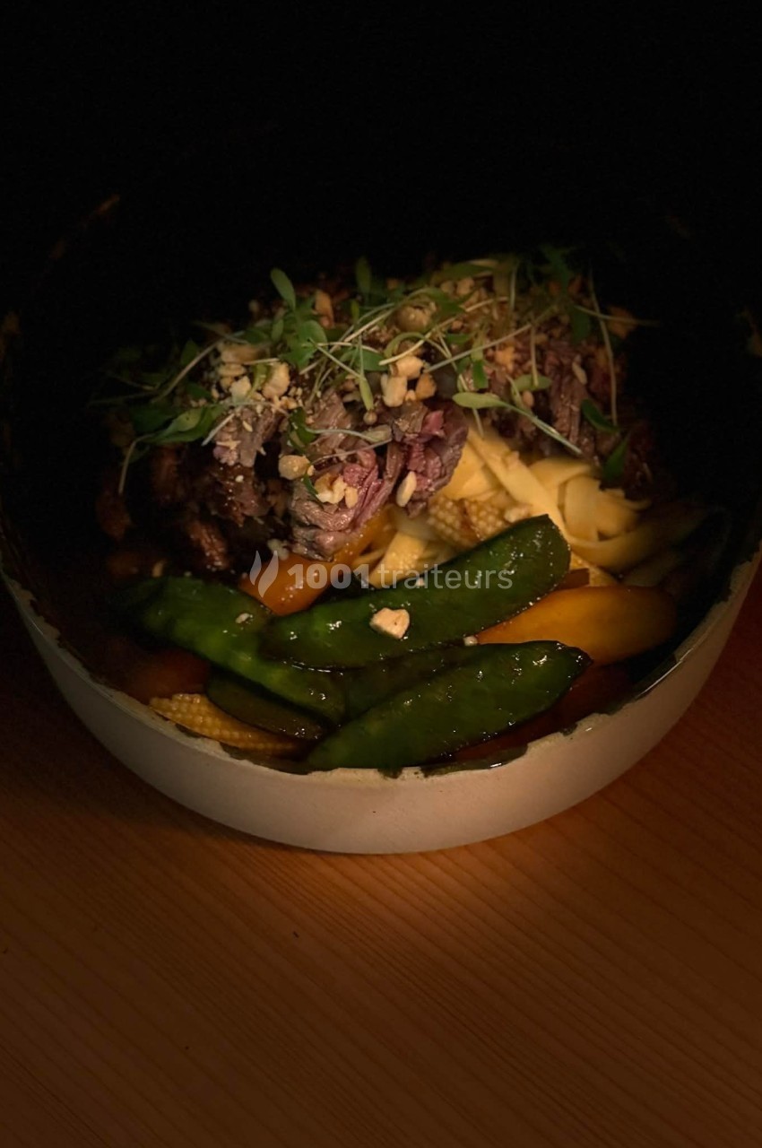 Bol de nouilles garni de légumes croquants, viande effilochée, herbes fraîches et éclats de noix.