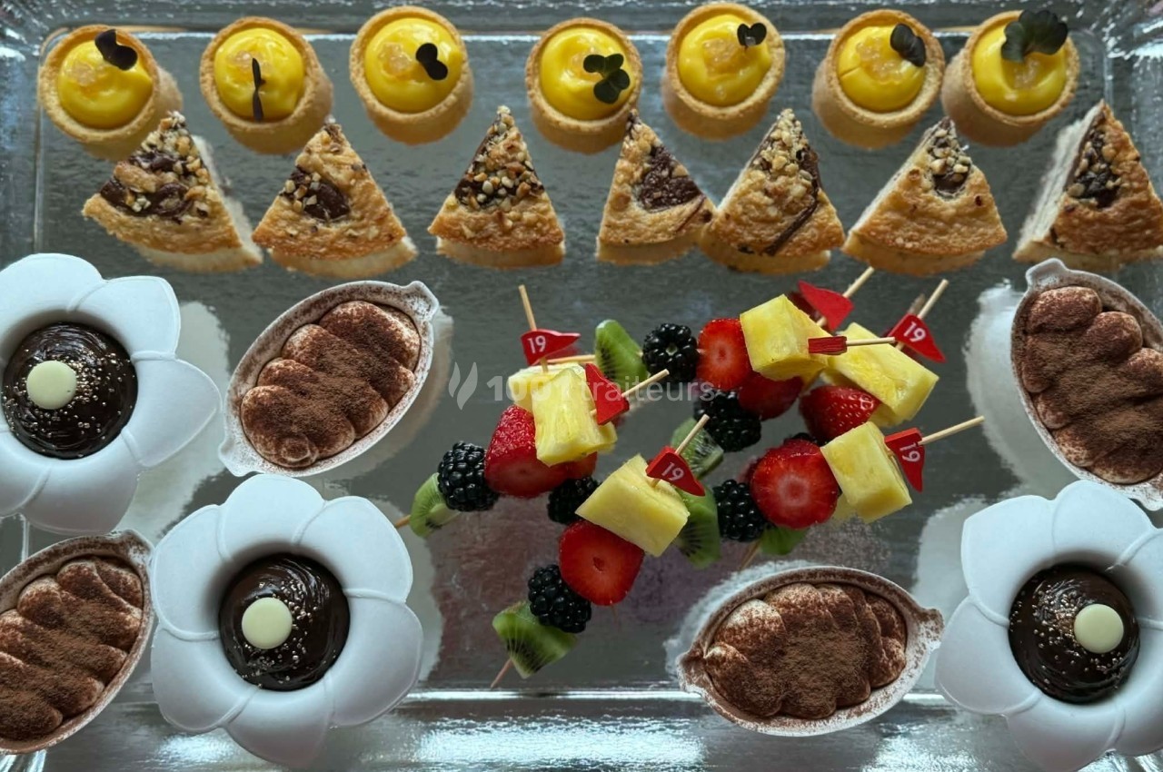 Plateau de desserts variés comprenant tartelettes, parts de gâteau, verrines et brochettes de fruits colorées.