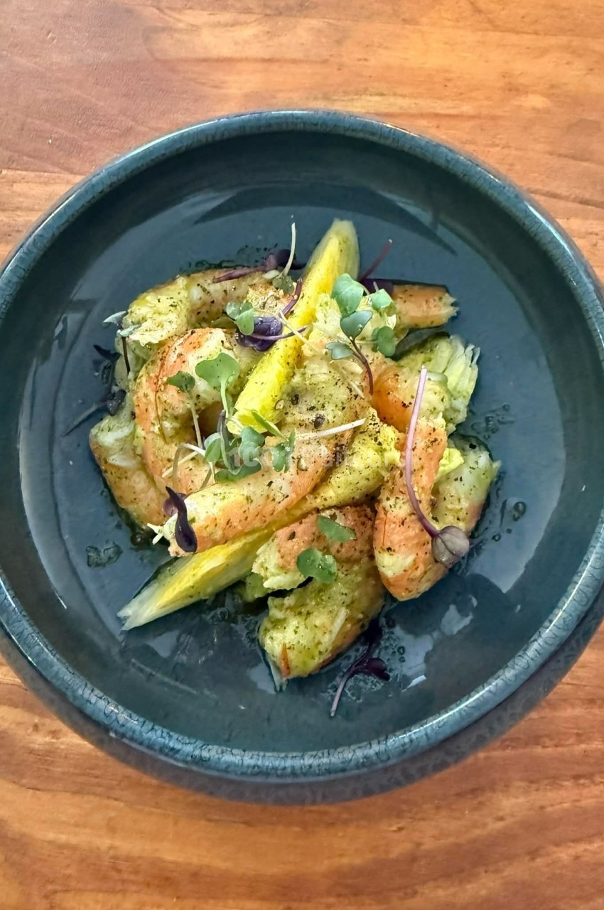 Assiette de crevettes marinées avec quartiers d'agrumes et jeunes pousses, servie sur une table en bois.