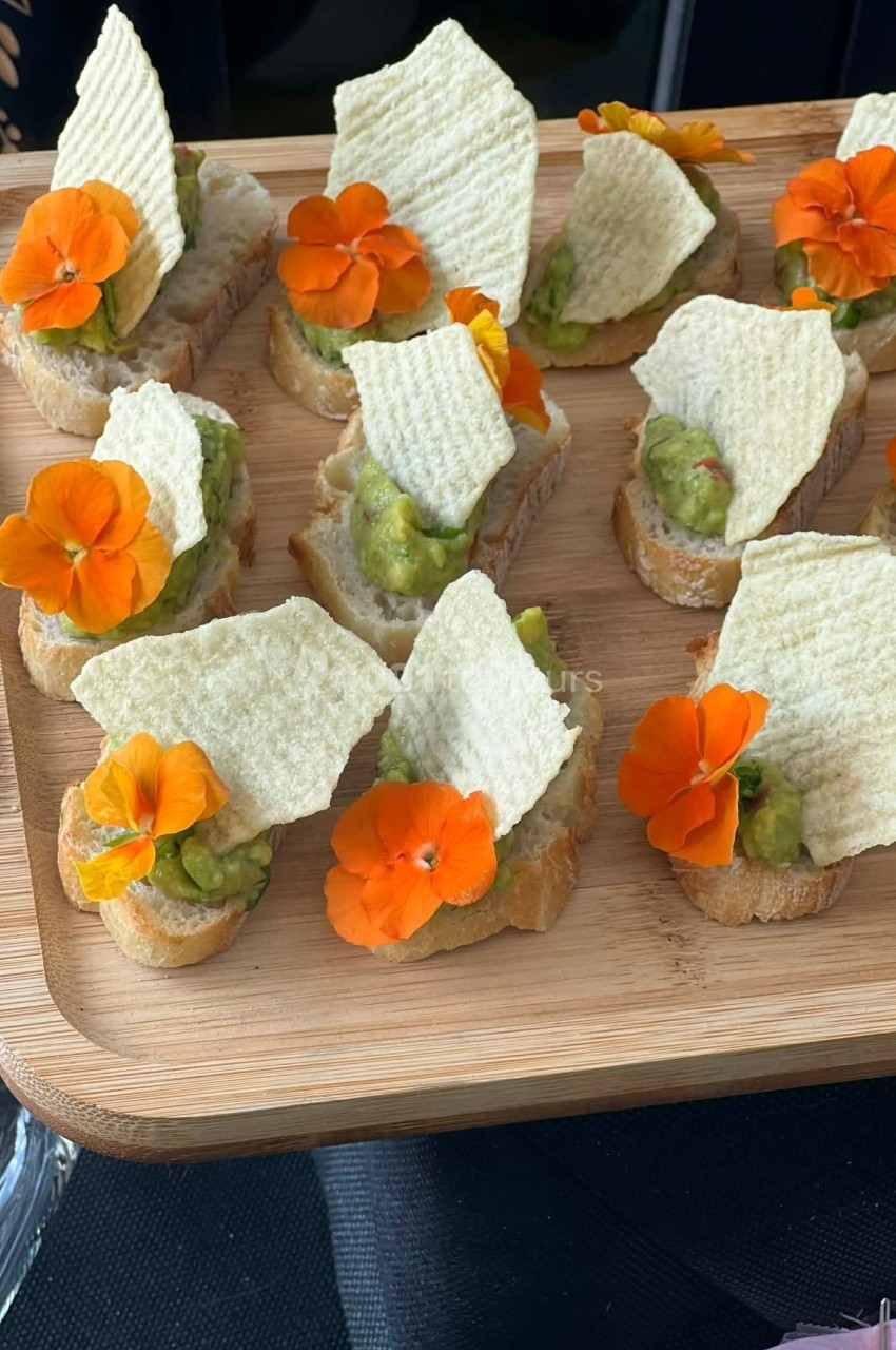 Plateau de toasts garnis de guacamole, chips et fleurs comestibles orange, présenté sur une planche en bois.