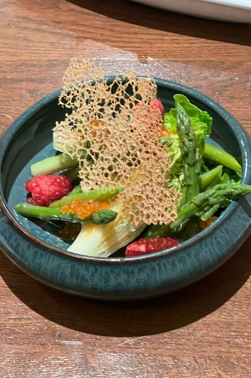 Assiette de légumes verts, framboises, œufs de poisson et tuile croustillante, présentée sur une table en bois.