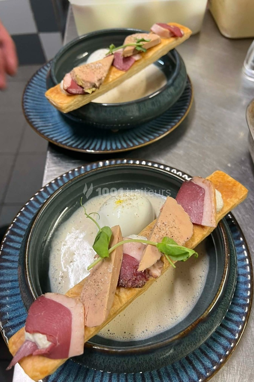 Deux assiettes avec une présentation gastronomique de tartes fines garnies de magret de canard, foie gras et herbes fraîches.