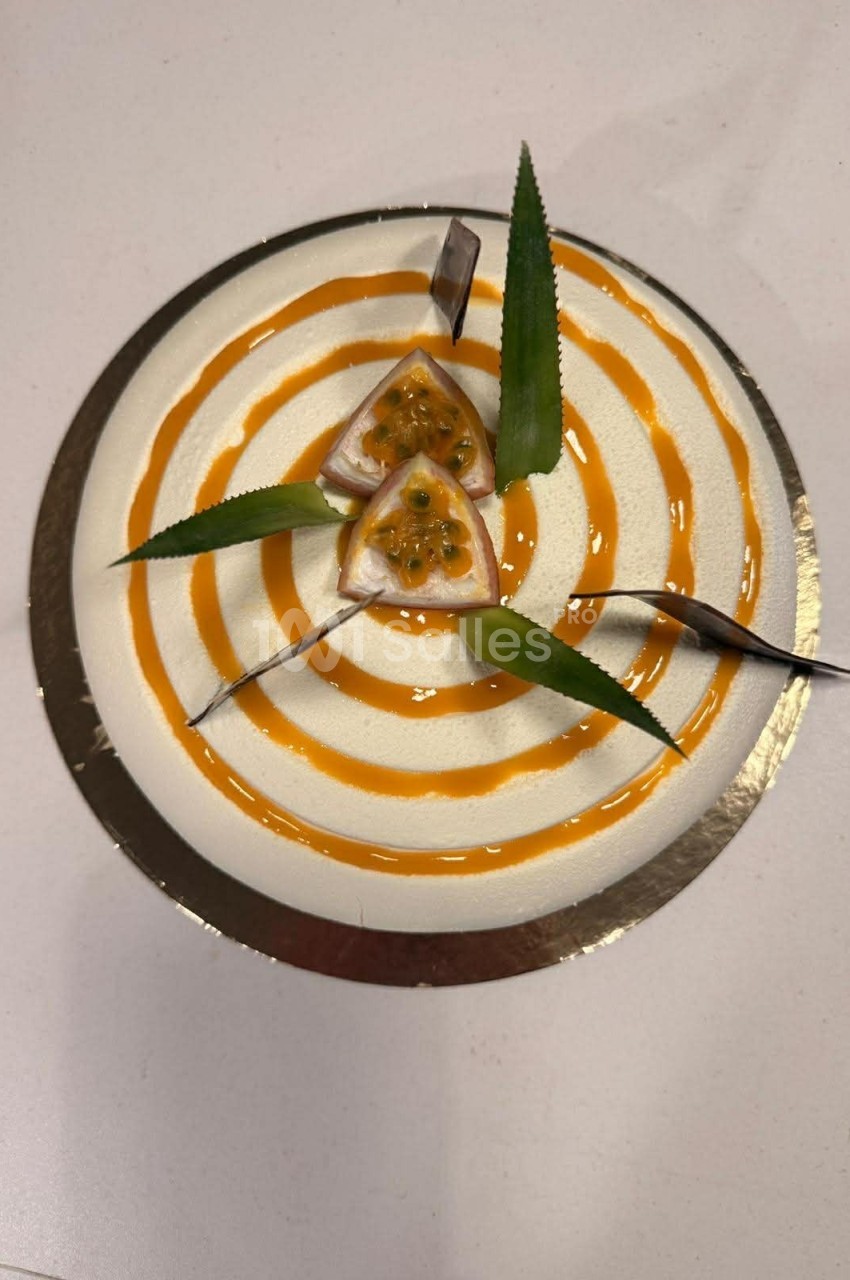 Gâteau rond décoré de spirales orange, morceaux de fruit de la passion et feuilles vertes sur le dessus.