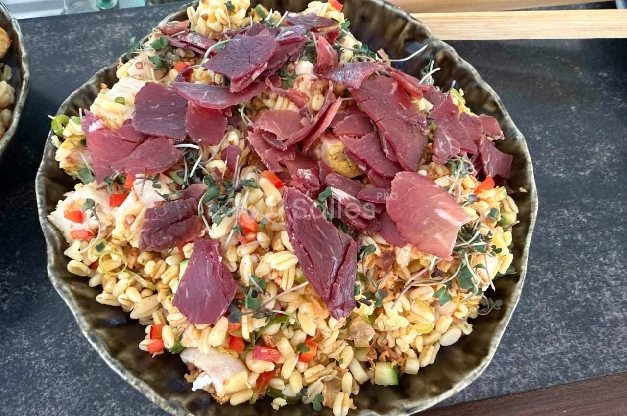 Assiette de salade de céréales garnie de tranches de viande séchée, légumes croquants et pousses fraîches.