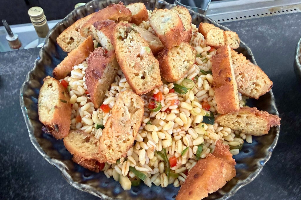 Salade de pâtes orzo avec légumes colorés et croûtons dorés dans un plat en céramique.