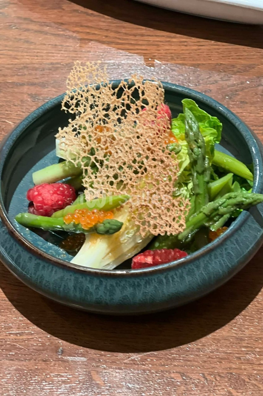Assiette de légumes verts, framboises, œufs de poisson et tuile croustillante, présentée sur une table en bois.