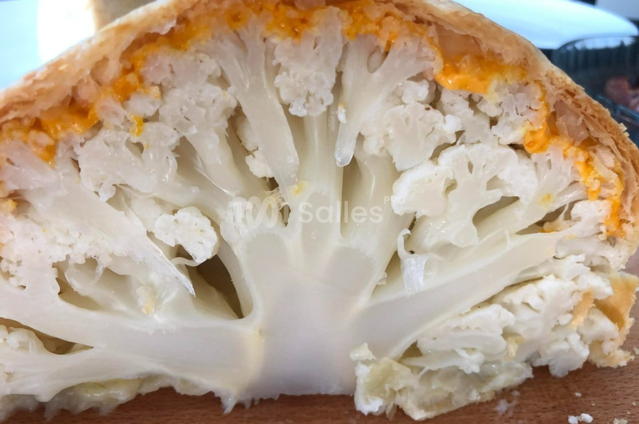 Chou-fleur entier cuit en croûte dorée, coupé en deux pour révéler l'intérieur tendre et légèrement gratiné.