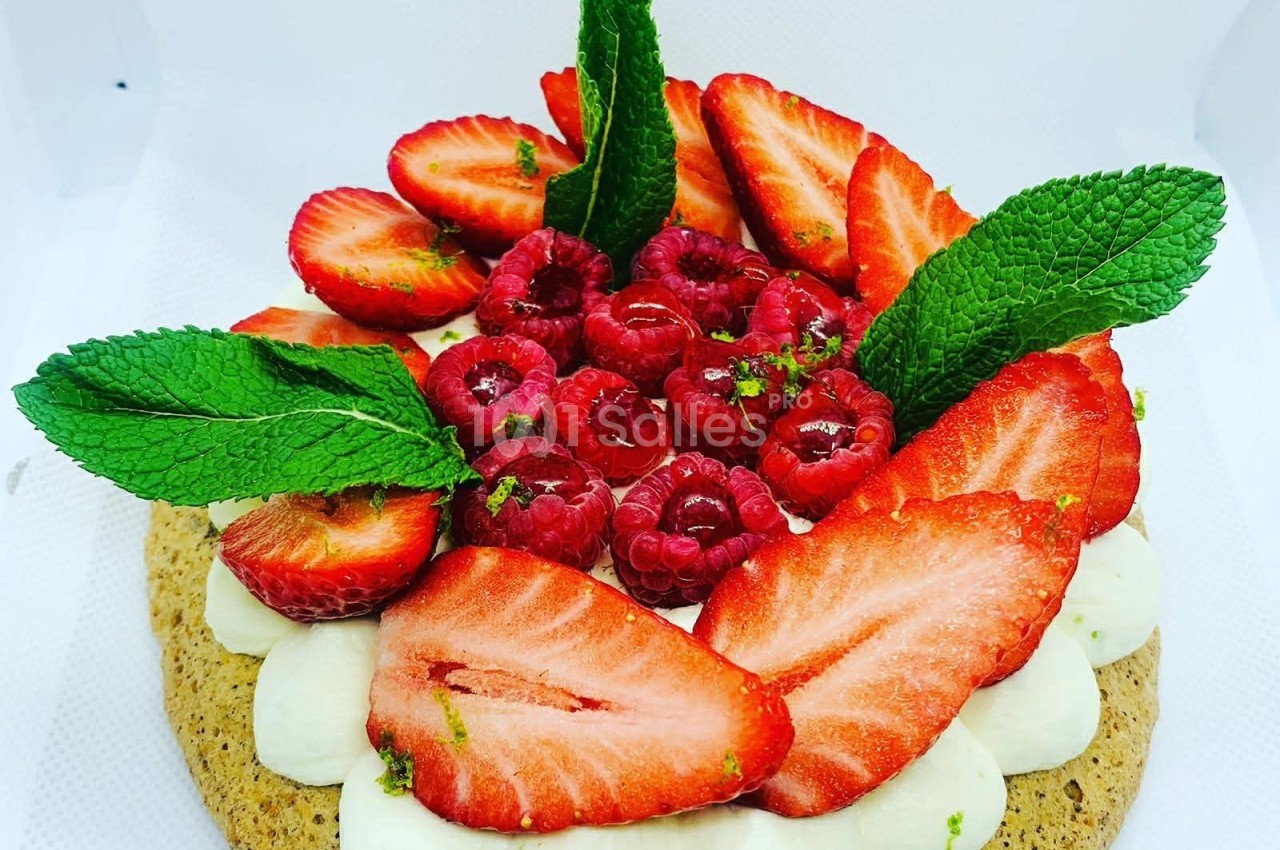 Tarte garnie de crème, fraises, framboises et feuilles de menthe, présentée sur un fond blanc.