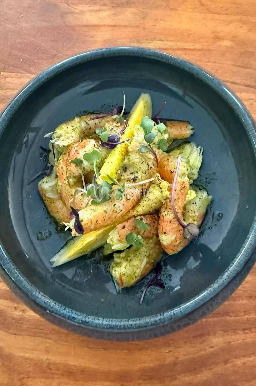 Assiette contenant des crevettes grillées, des morceaux d'agrumes et des micro-pousses, présentée sur une table en bois.
