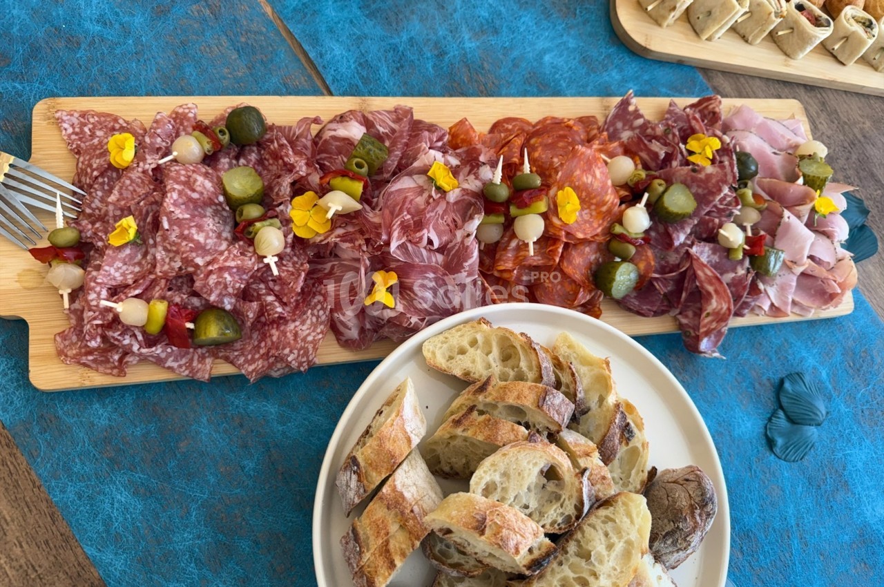 Plateau de charcuterie variée avec cornichons et fleurs comestibles, accompagné de tranches de pain.