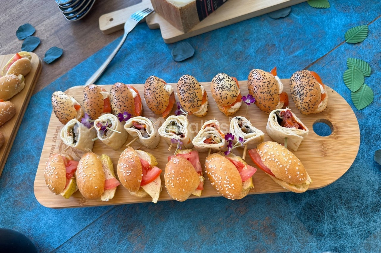 Plateau en bois avec mini-sandwichs garnis de légumes et wraps roulés, disposés pour un buffet ou un apéritif.