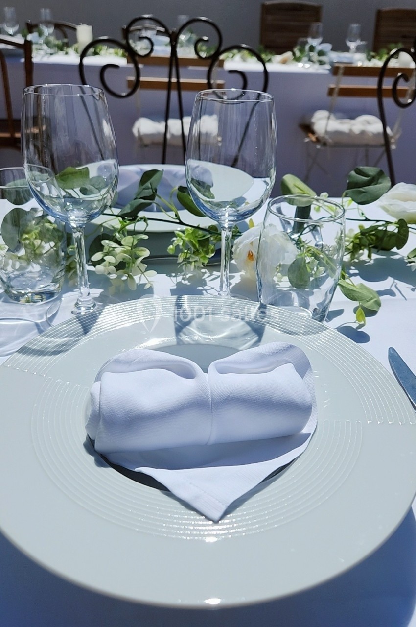 Table dressée avec une assiette blanche, une serviette pliée, des verres et une décoration florale élégante.