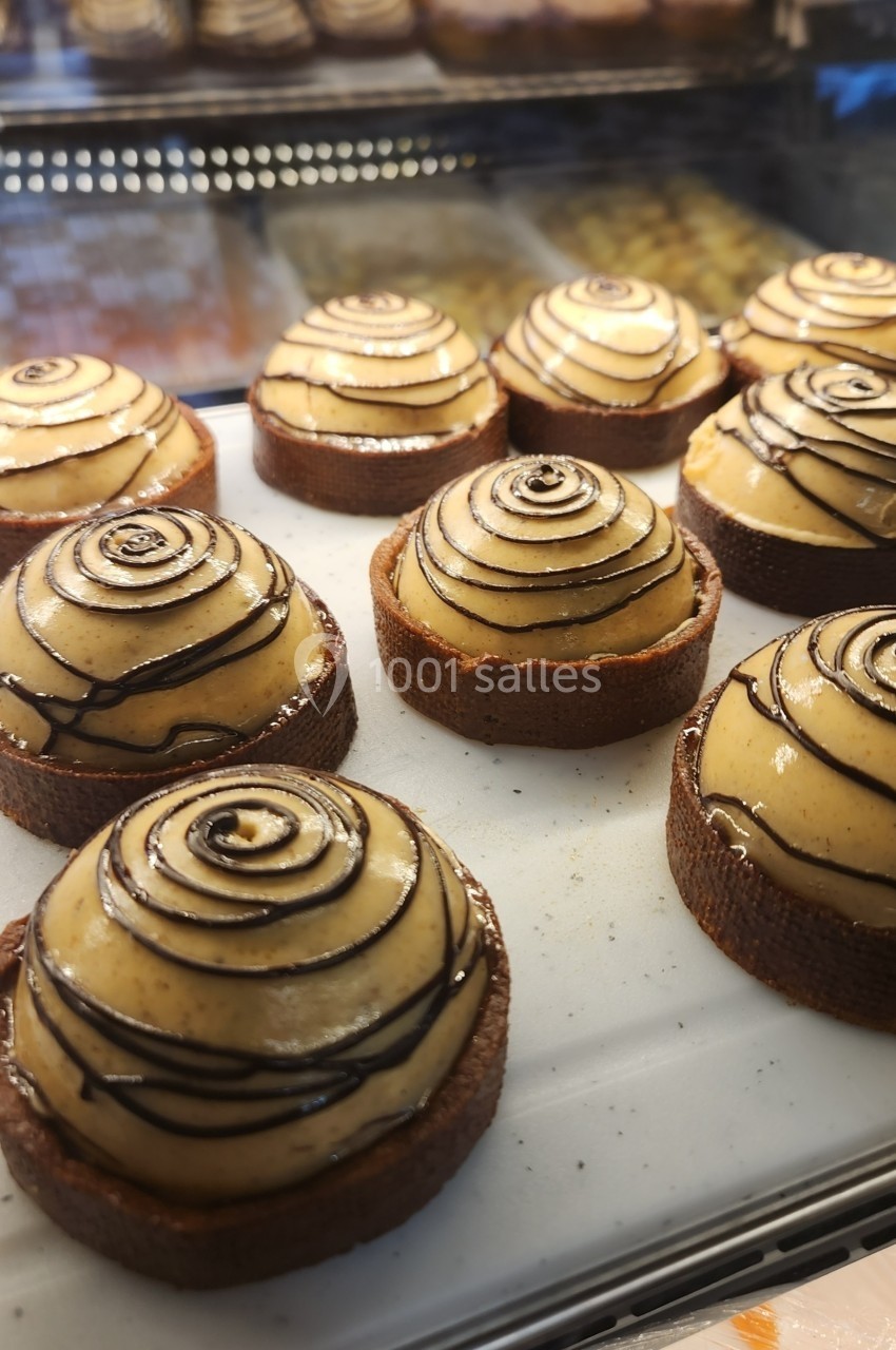 Tartelettes garnies de crème vanillée et décorées de spirales de chocolat, exposées sur un présentoir en pâtisserie.