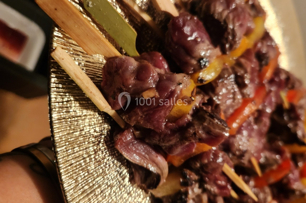 Brochettes de viande grillée avec des morceaux de poivrons colorés, servies sur une assiette dorée.