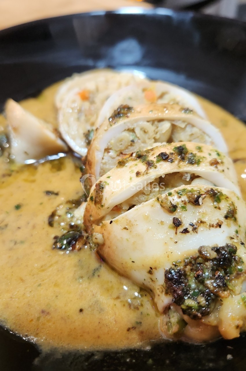 Calamar farci servi dans une sauce crémeuse aux herbes, présenté dans une assiette noire.