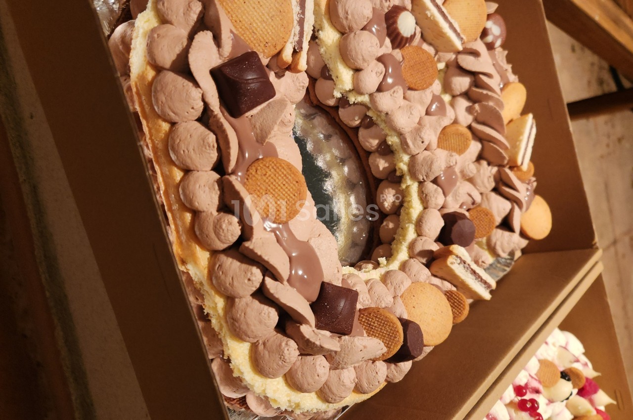 Gâteau en forme de couronne décoré de crème chocolatée, biscuits et morceaux de chocolat.