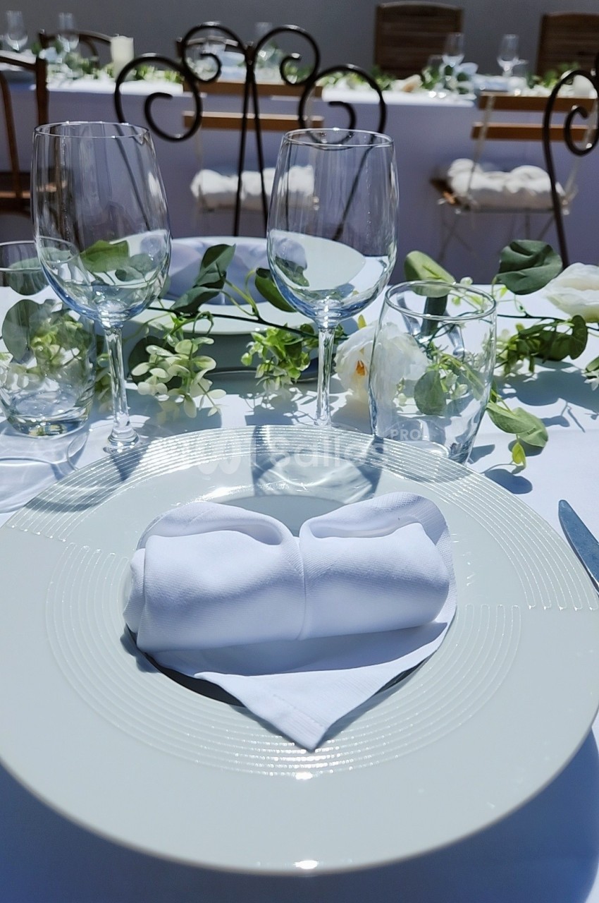 Table dressée avec une assiette blanche, une serviette pliée, des verres et une décoration florale élégante.