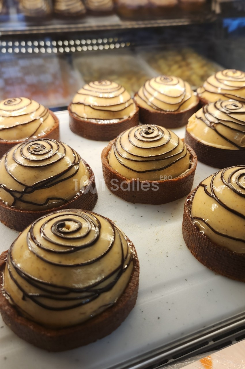 Tartelettes garnies de crème vanillée et décorées de spirales de chocolat, exposées sur un présentoir en pâtisserie.