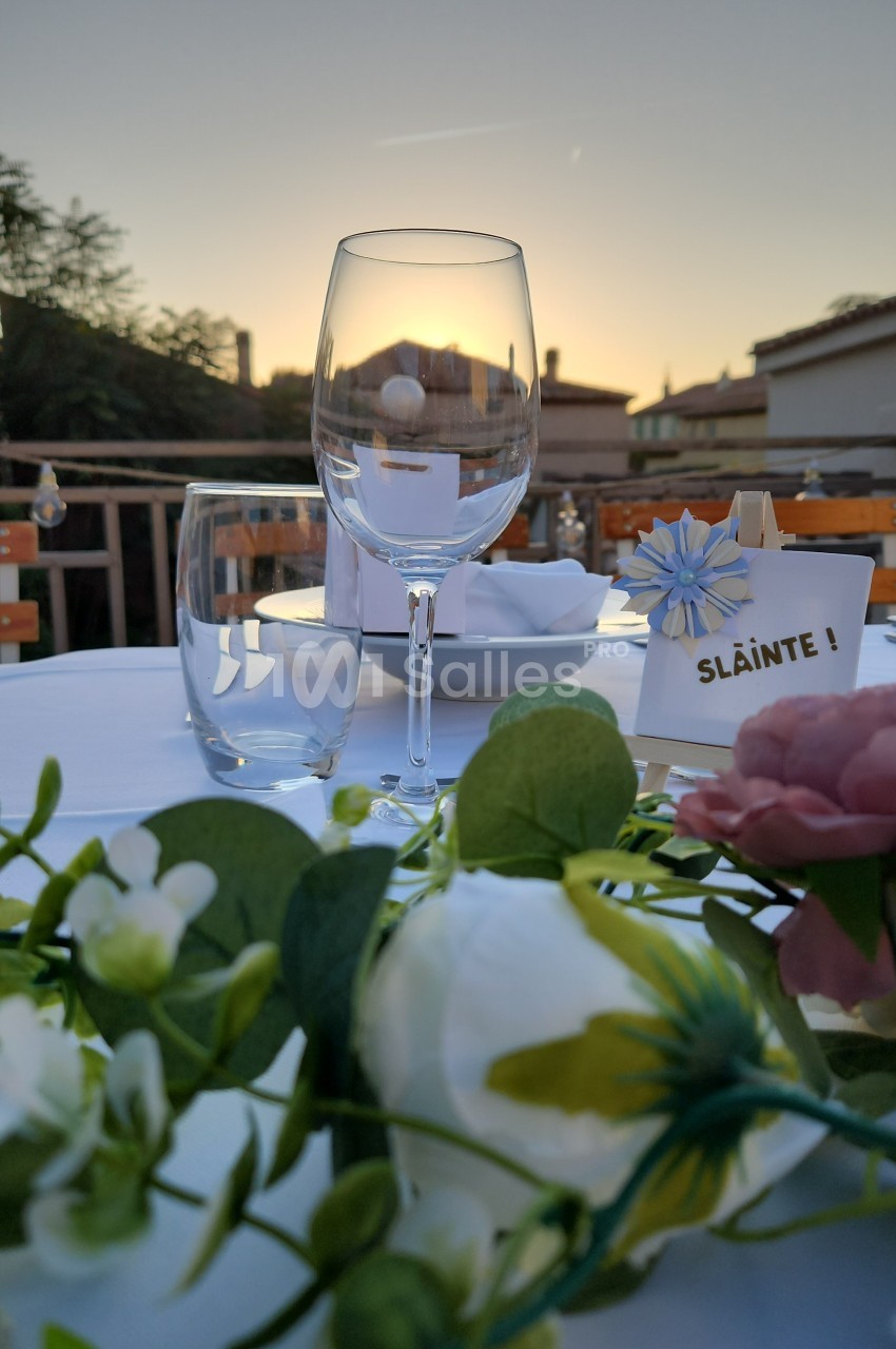 Verres et décorations florales sur une table dressée en extérieur au coucher du soleil.