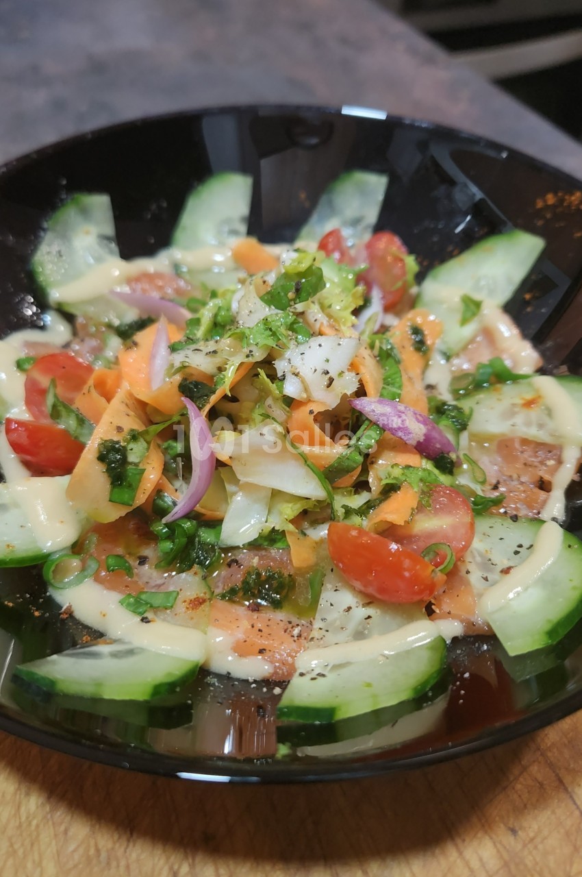 Salade colorée avec concombres, tomates cerises, carottes râpées, oignons rouges et herbes, servie dans un bol noir.