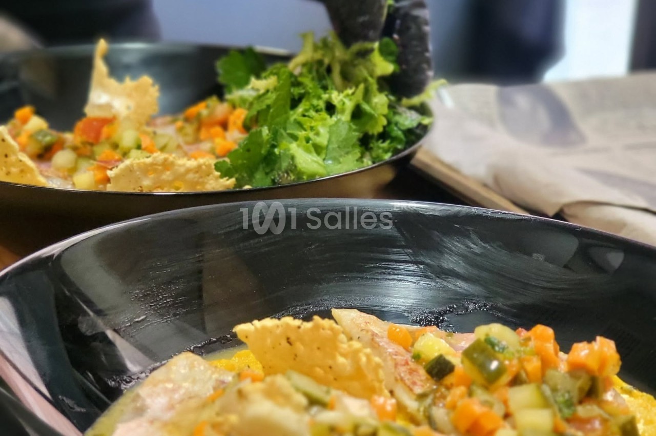 Un chef ajoute des herbes fraîches à des assiettes garnies de légumes en dés et de chips croustillantes.