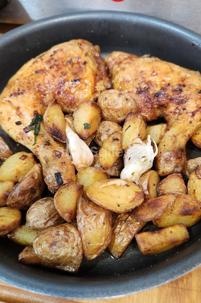 Poulet rôti avec des pommes de terre dorées et de l'ail dans une poêle noire.