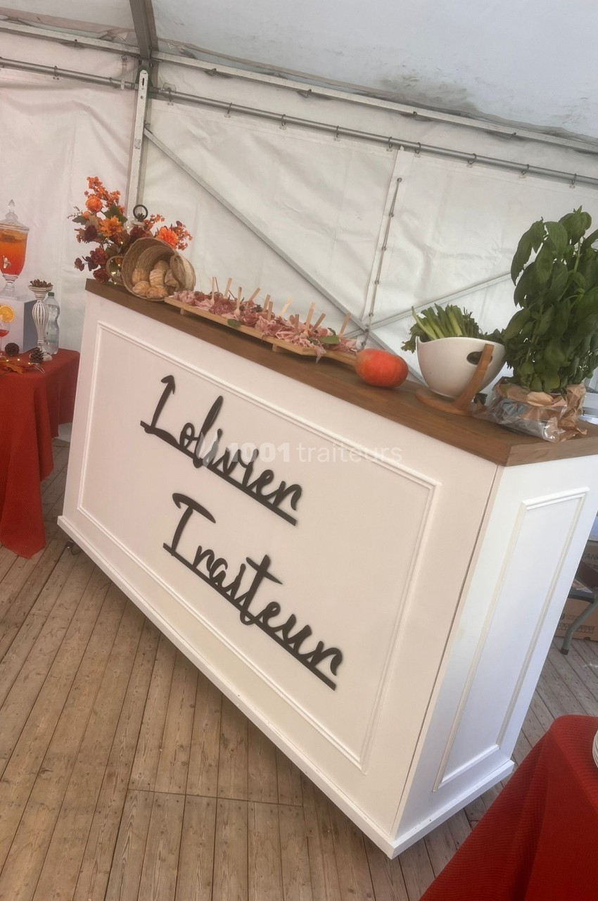 Comptoir de traiteur décoré avec des aliments, herbes fraîches et éléments automnaux sous une tente blanche.
