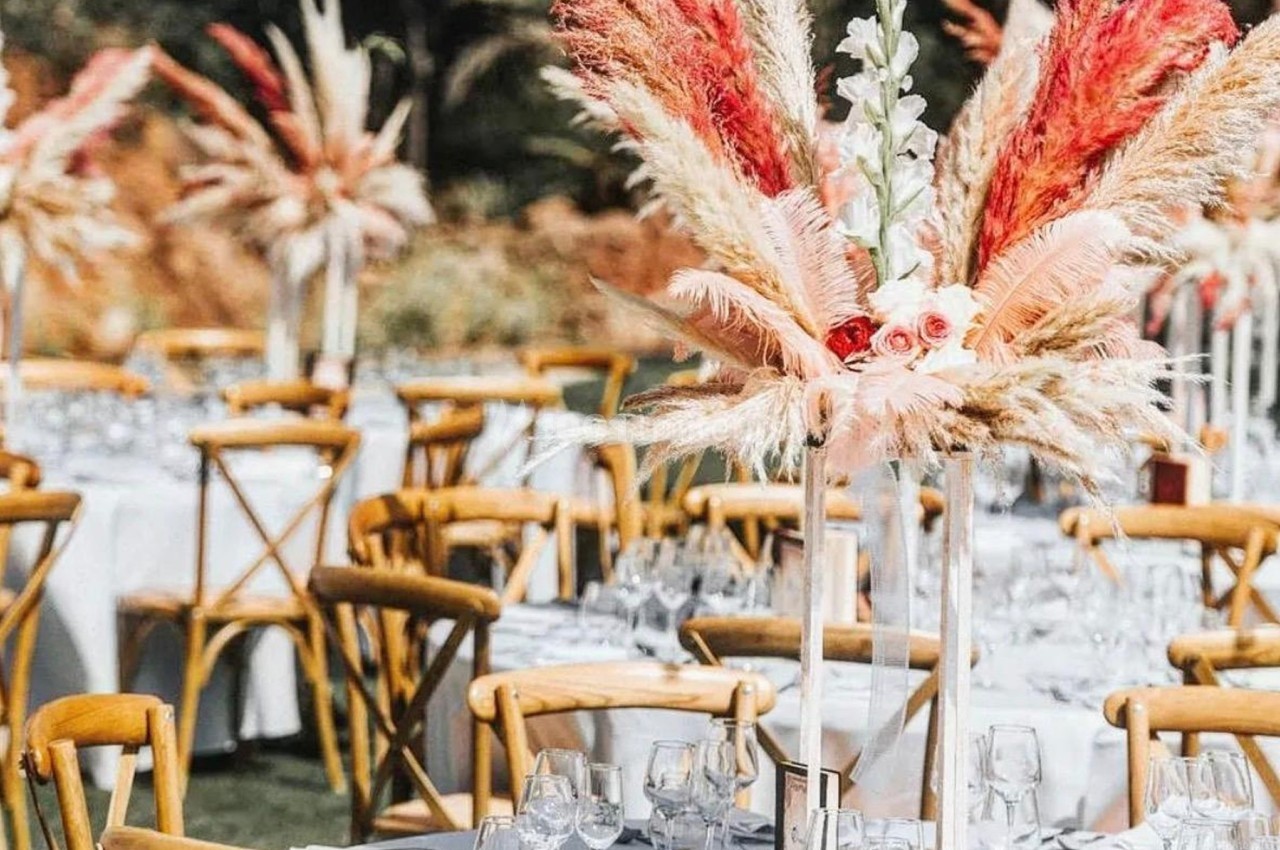Tables de réception en extérieur décorées de centres de table avec des fleurs et des herbes séchées colorées.