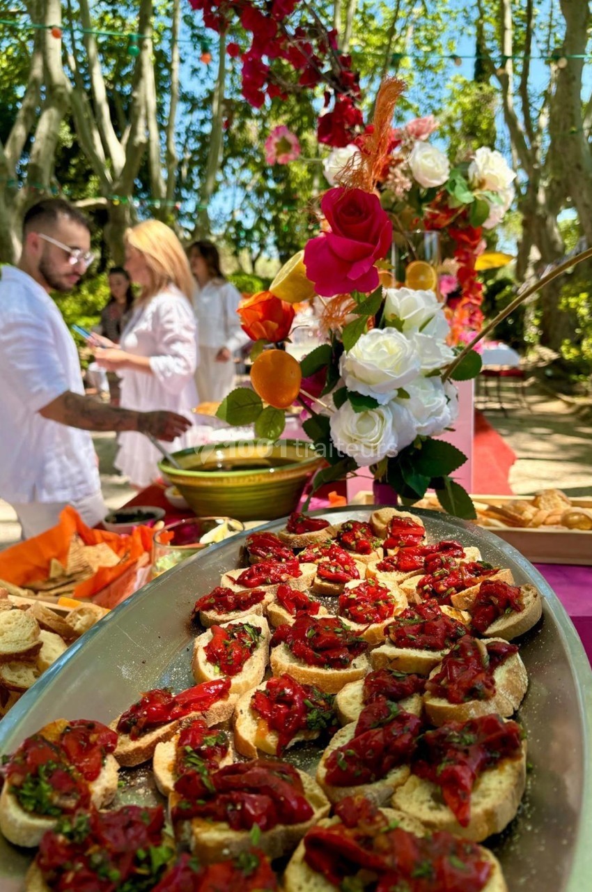 Plateau de bruschettas garnies de tomates et herbes fraîches, disposé sur une table en extérieur décorée de fleurs.