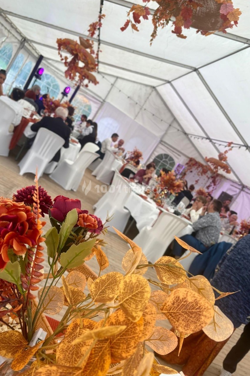 Invités assis dans une tente décorée de fleurs et feuilles d'automne pour un événement festif.