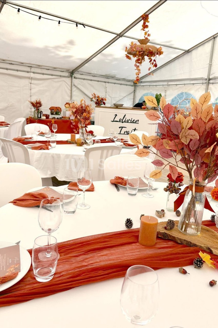 Tables décorées dans une tente, ornées de feuilles d'automne, bougies et nappes rouges pour un événement festif.