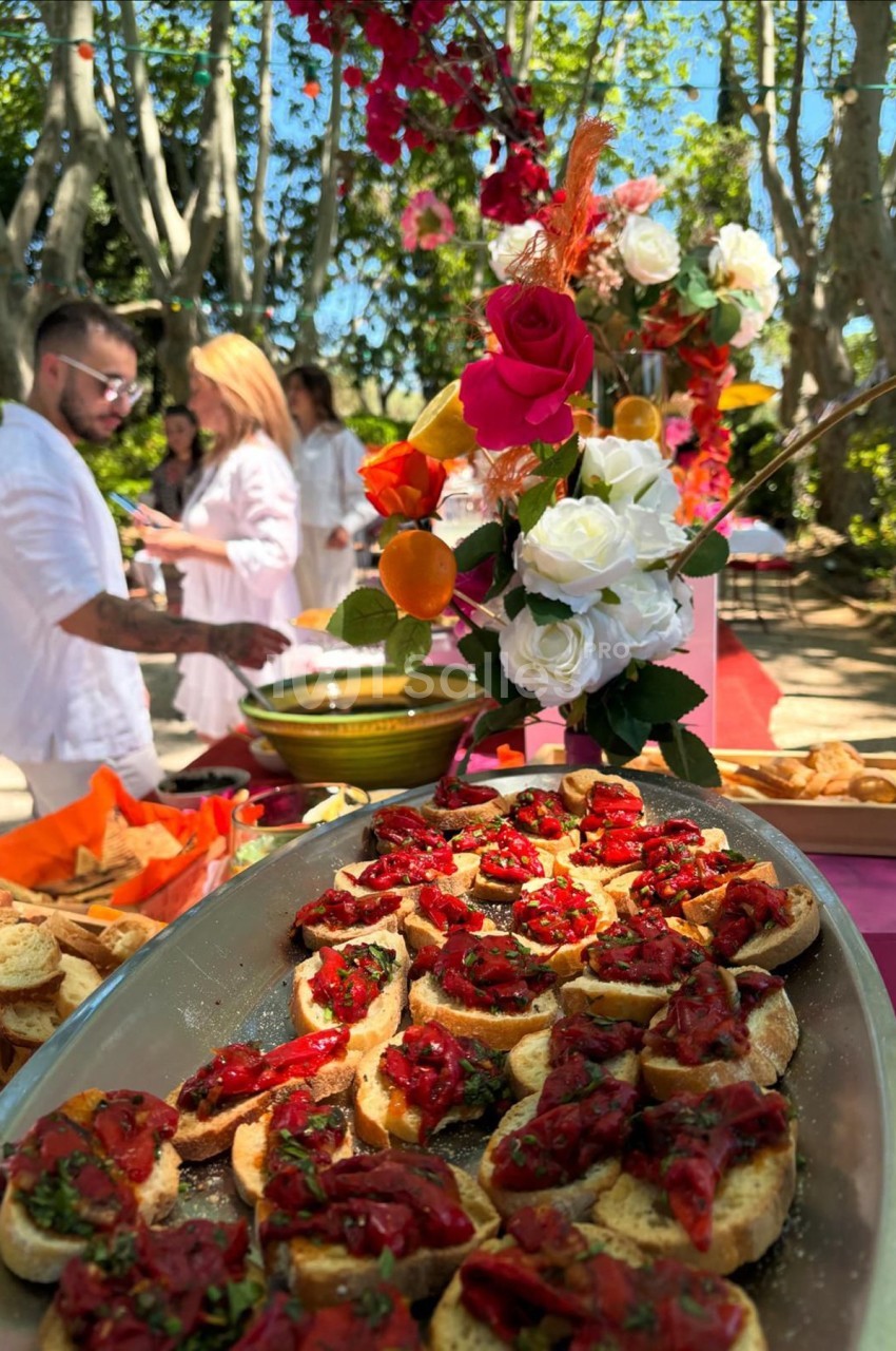 Plateau de bruschettas garnies de tomates et herbes fraîches, avec un décor floral en arrière-plan dans un jardin.