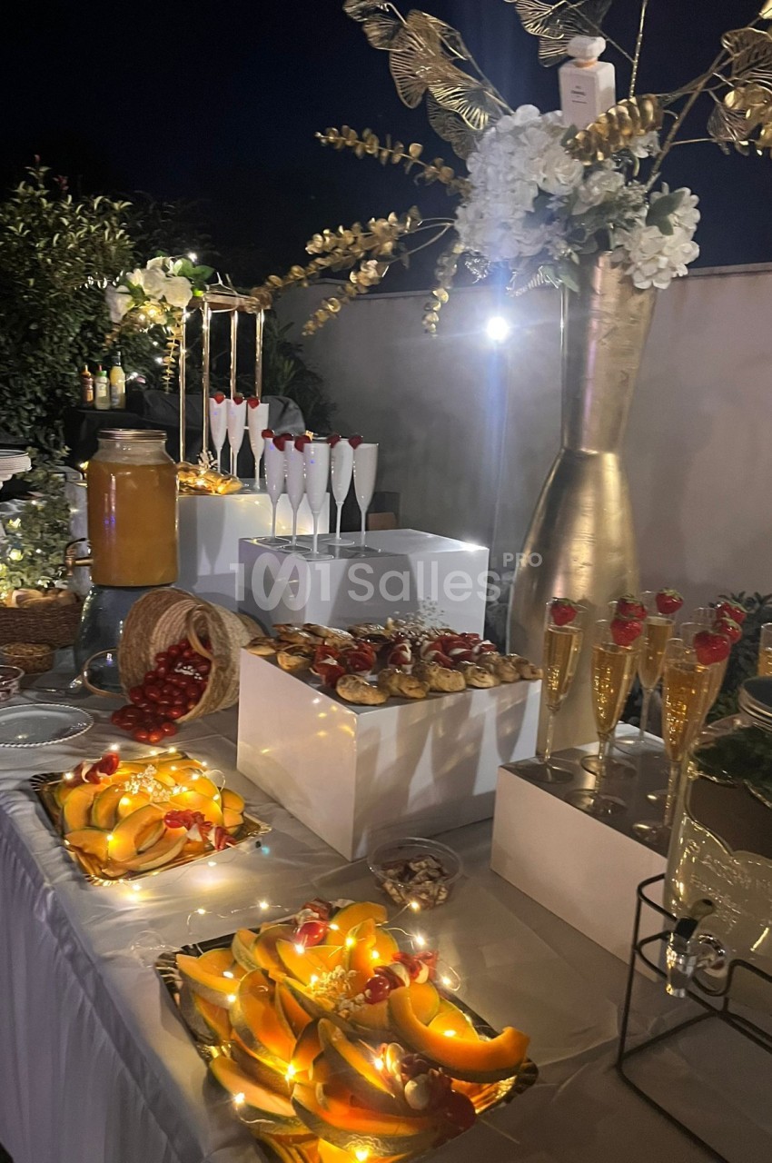Table de buffet élégamment décorée avec des fruits, pâtisseries, boissons et guirlandes lumineuses, en extérieur nocturne.