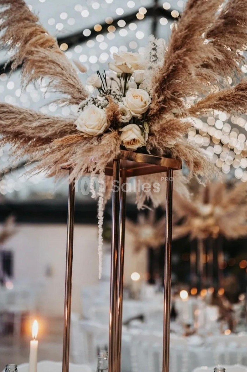 Centre de table avec des pampas, des roses blanches et des lumières suspendues dans une ambiance de soirée festive.
