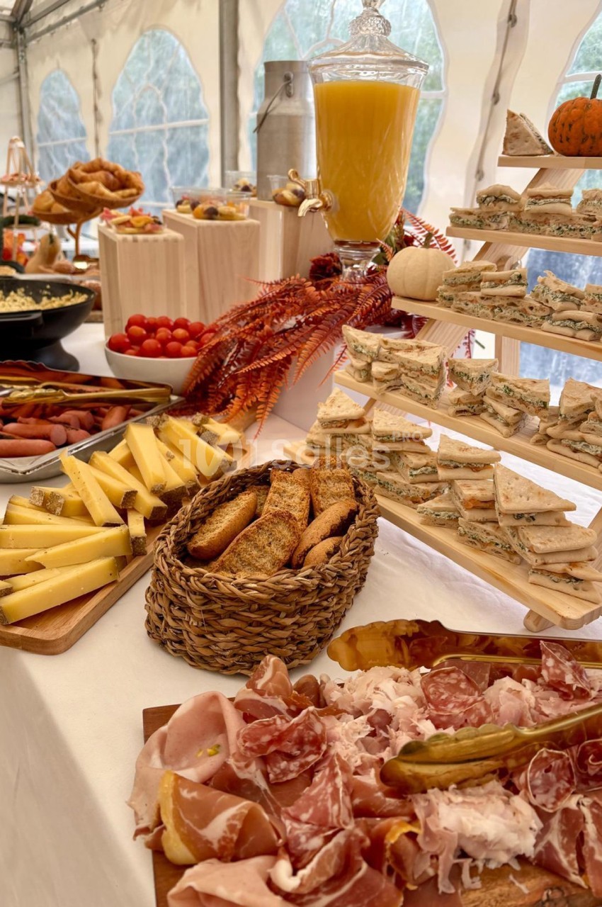 Buffet varié avec charcuterie, fromages, pains, sandwichs et jus d'orange, disposé sur une table décorée.