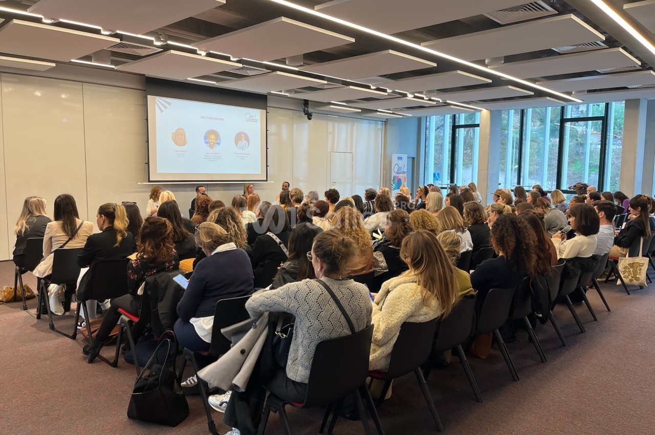 Salle de conférence avec un public attentif, regardant une présentation projetée sur un écran.