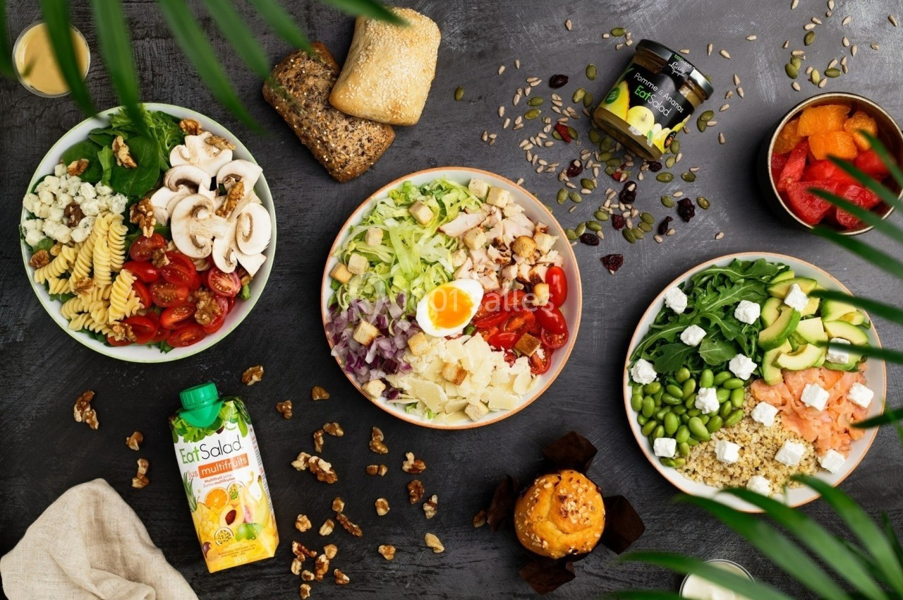 Assortiment de salades variées avec légumes, noix, pain et boissons sur une table sombre décorée de feuilles.