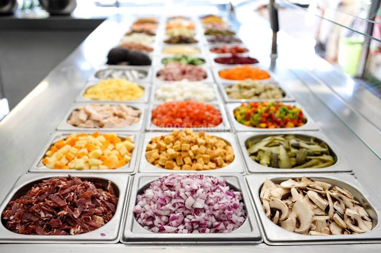 Bacs remplis d'ingrédients variés comme légumes, viandes et fromages, disposés sur un comptoir de préparation.