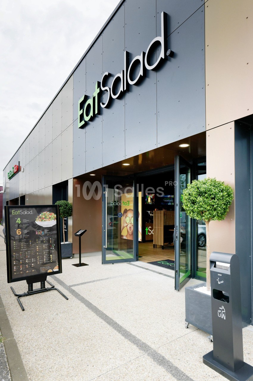 Façade d'un restaurant avec enseigne ’Eat Salad’, entrée vitrée, menu extérieur et poubelle à proximité.