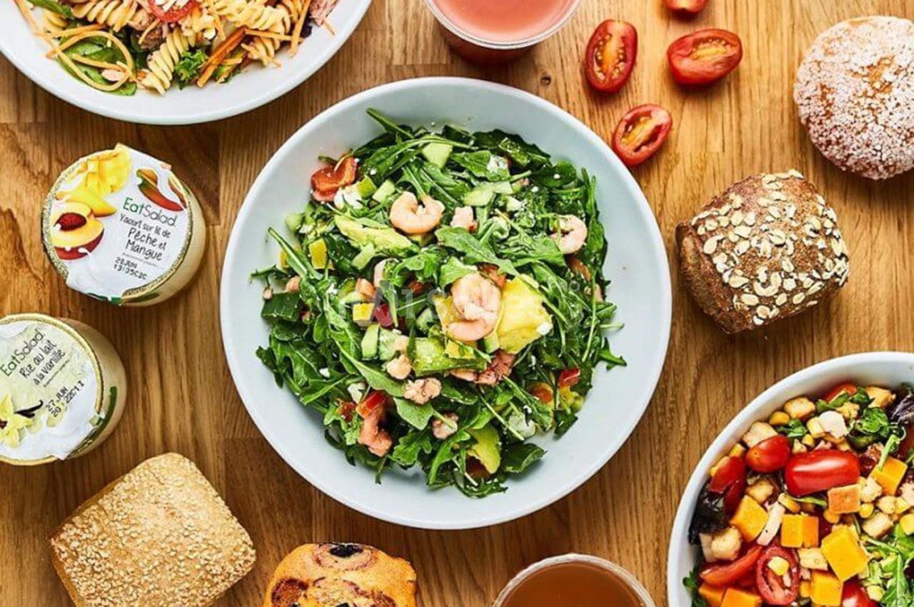 Assortiment de plats et aliments variés sur une table en bois, incluant salade, pain, fruits et boissons.