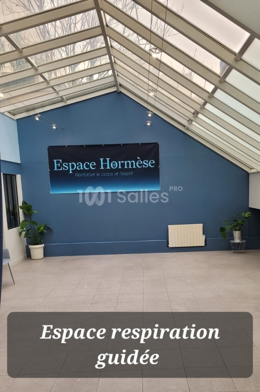 Salle lumineuse avec verrière, murs bleus, plantes et panneau ’Espace Hormèse’ sur le mur du fond.